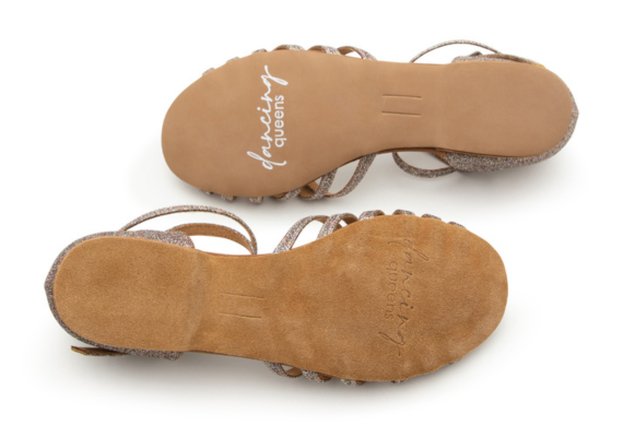 Zwei hellbraune Tanzschuhe, die von den Sohlen her gezeigt werden und auf denen in Schreibschrift "dancing queens" steht.